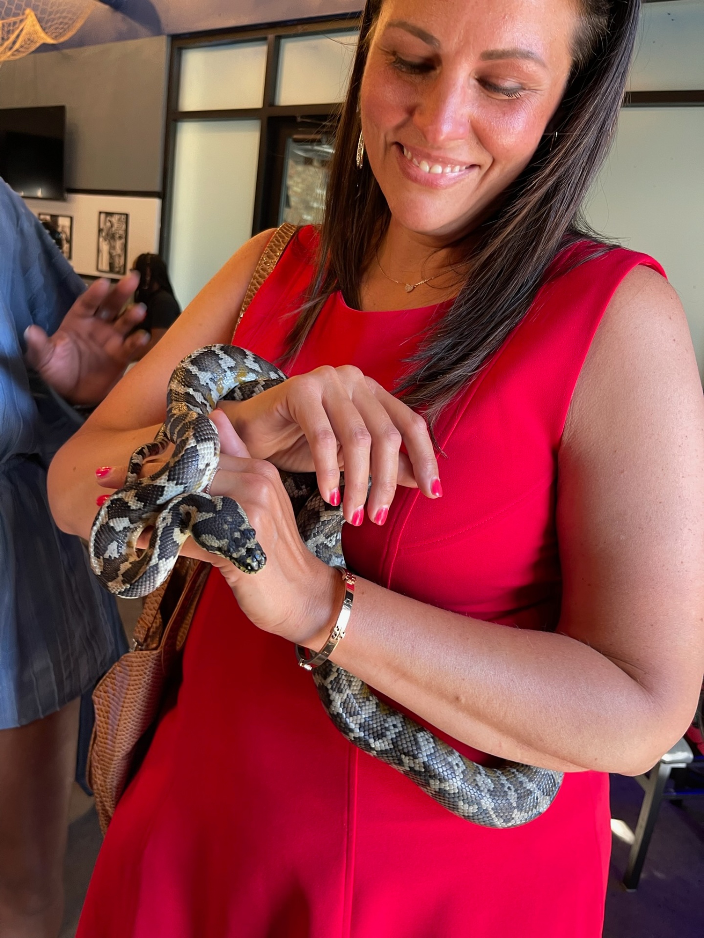 A smiling attendee holding a ball python at an All My Creatures event.