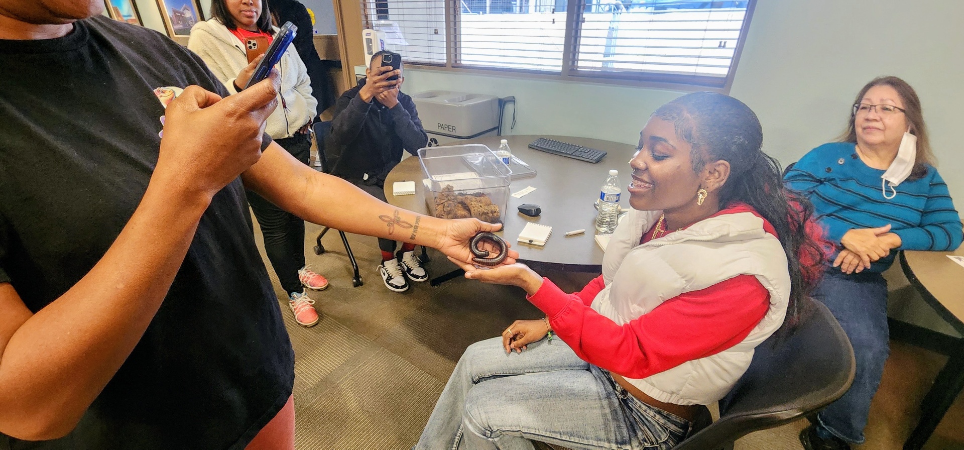 CJ smiling as she holds a millipede out for a young participant to see up close.