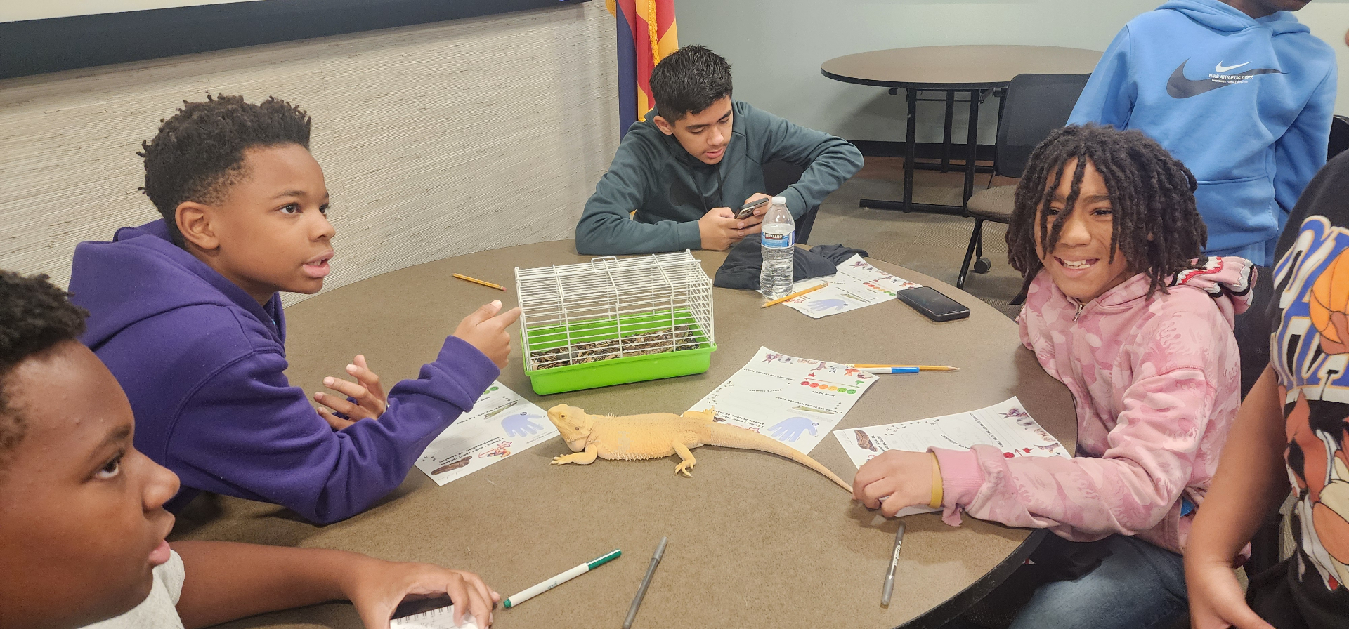 Kids gathered around a bearded dragon on the table, learning together.