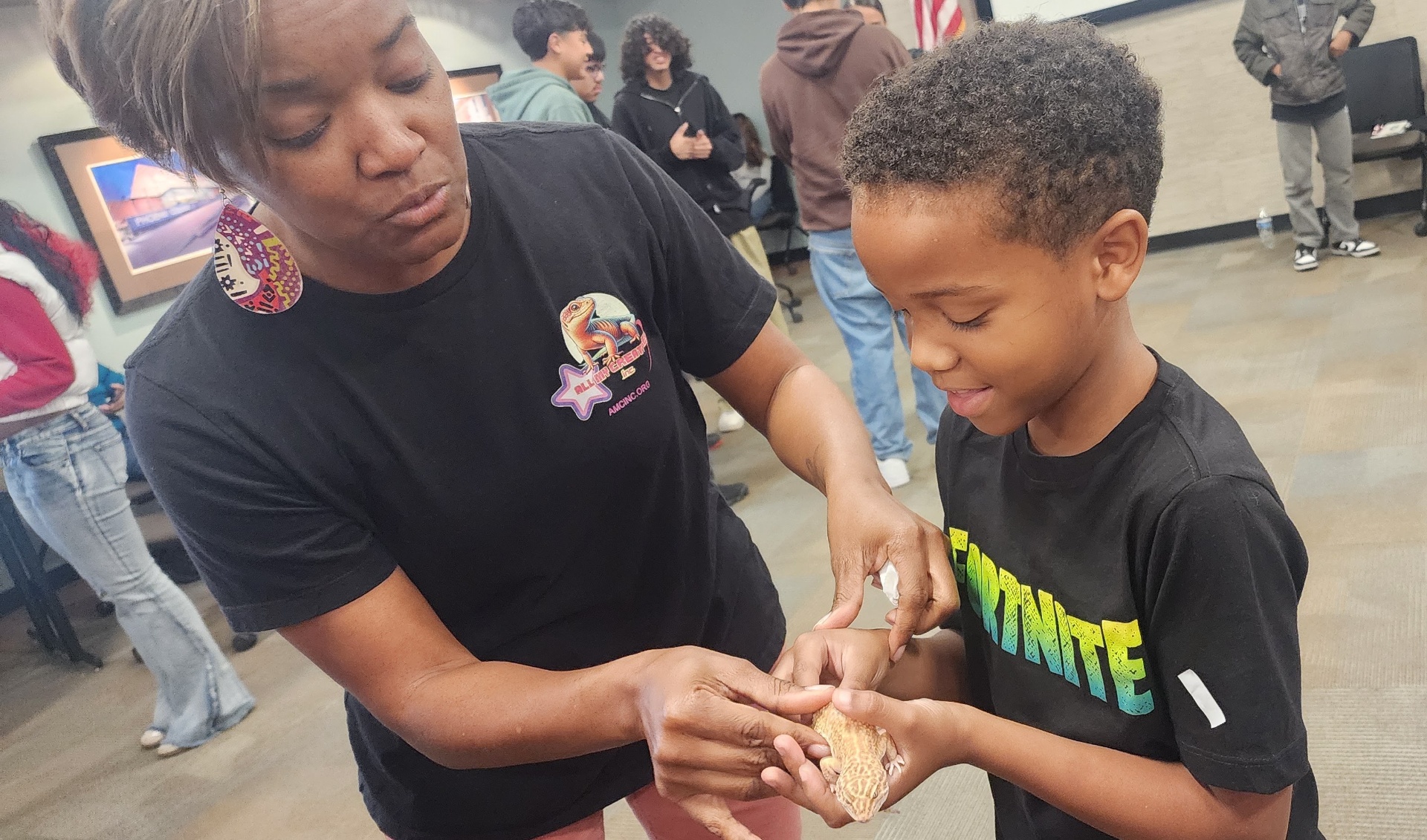 CJ gently helping a young boy hold a leopard gecko during a school visit.